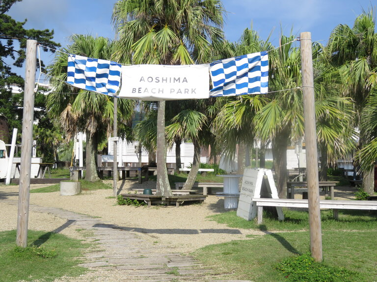Entrance to Aoshima Beach Park with a sign and palm trees in the background.
