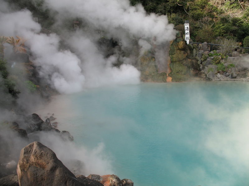 A scenic view of a hot spring surrounded by steam and rocks, with a sign in the background.
