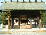 A traditional Japanese shrine building with a wooden roof and entrance, surrounded by greenery.