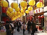 A bustling street in Nagasaki, Japan, adorned with vibrant yellow lanterns and lined with shops, showcasing a lively atmosphere as people walk through.