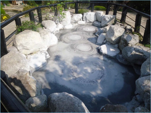A mineral-rich hot spring surrounded by stones, with steam rising from the surface.