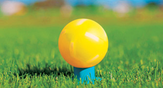 A close-up image of a yellow park golf ball resting on a blue tee on green grass.
