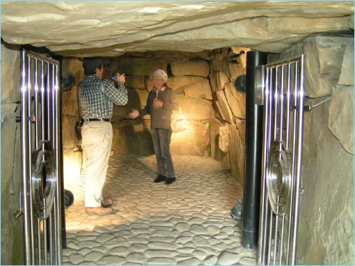 Interior view of a burial mound at Saitobaru, featuring stone walls and a couple standing inside, with one person taking a photo.