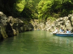 Scenic view of the Takachiho gorge with lush green trees lining the rocky cliffs and a calm river, where people are enjoying boating.
