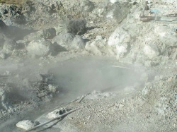 A geothermal hot spring with steam rising in a rocky landscape.