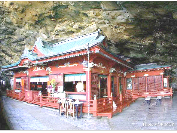 Traditional Shinto shrine built within a cave on a coastal cliff, featuring intricate red and gold decorations.