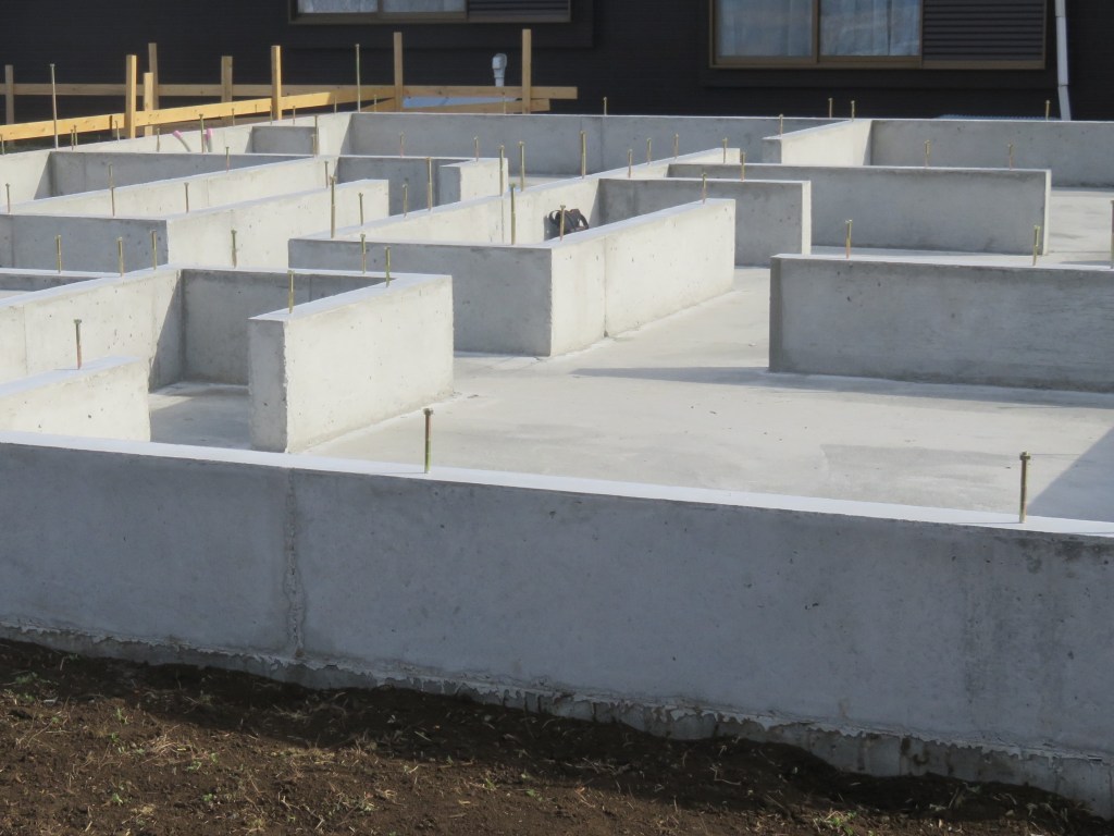 Concrete foundation for a house under construction, featuring steel reinforcement bars and a grid-like layout.