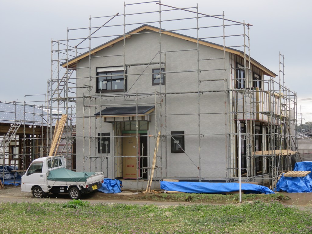 A house under construction in Japan, surrounded by scaffolding, with materials and a small vehicle parked nearby.