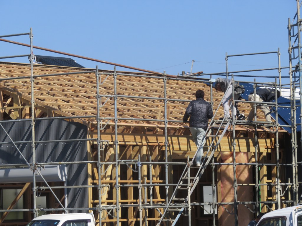 Workers constructing a wooden house using scaffolding, showcasing the process of building in Japan.