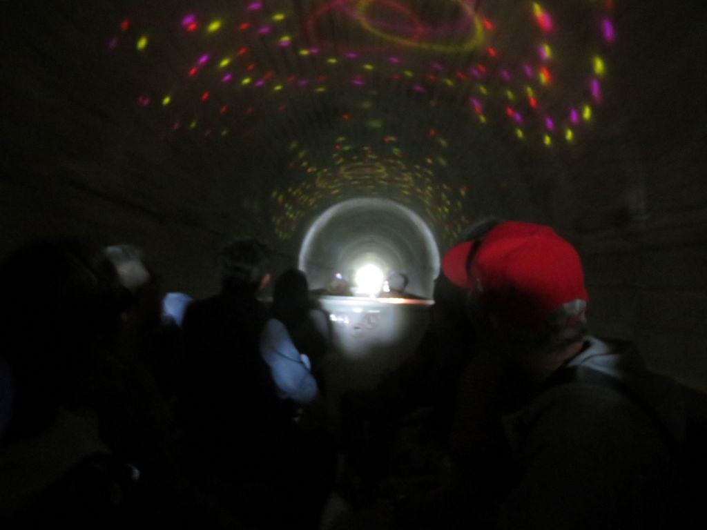 Visitors viewing light projections inside a dimly lit tunnel, with colorful patterns reflecting on the walls.