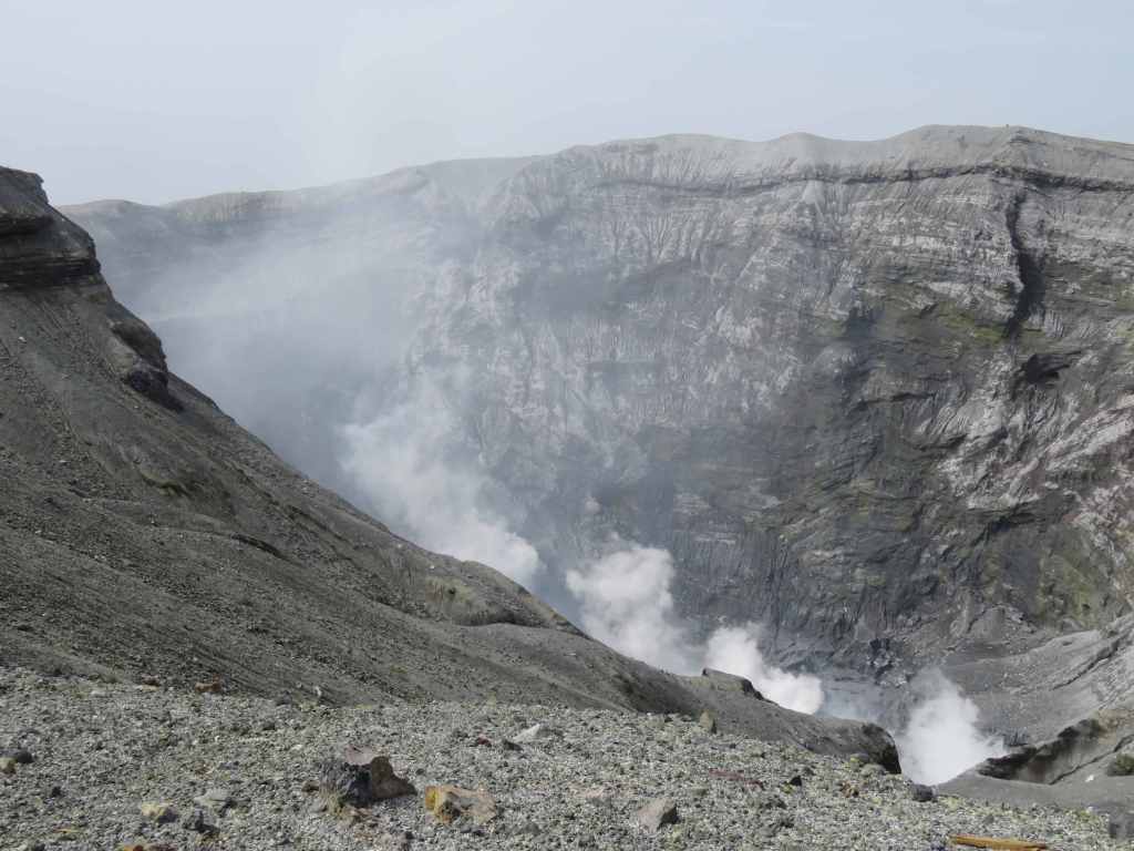 Aerial view of the active crater of Mount Aso, showcasing steam and volcanic rock formations.